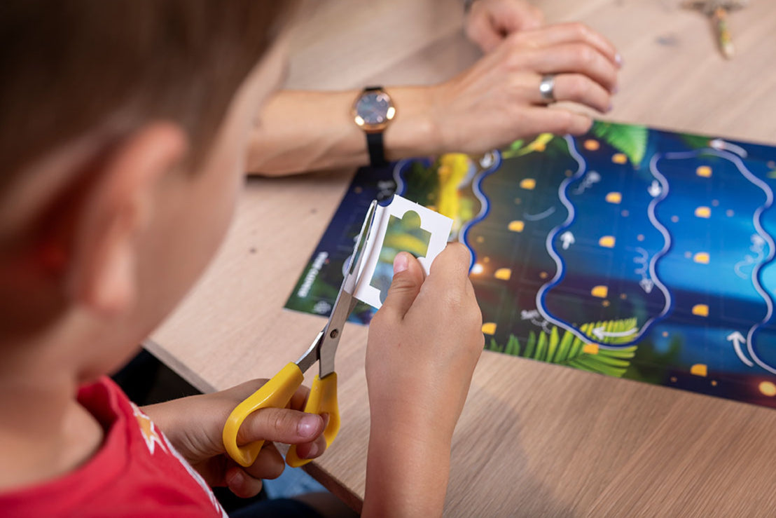 Kind schneidet mit Schere ein Puzzlestück aus dem Dino-Kalender